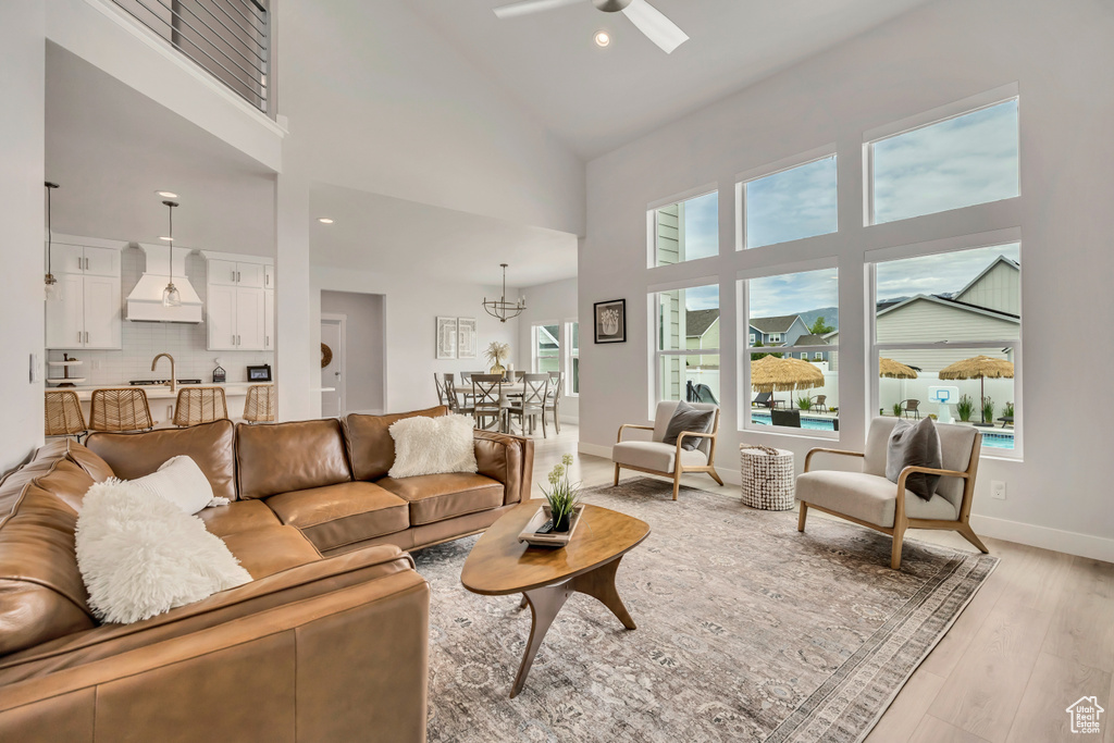 Living area featuring a ceiling fan, high vaulted ceiling, light wood-type flooring, healthy amount of natural light, and baseboards