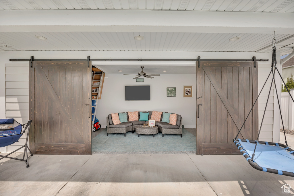 Living room with a barn door, a ceiling fan, and beam ceiling