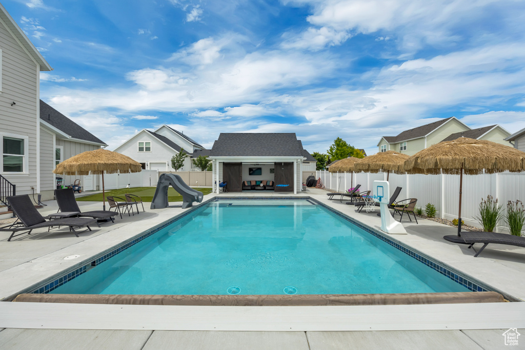 View of swimming pool featuring a water slide, a fenced backyard, a storage structure, and a patio area
