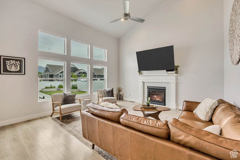 Living area with high vaulted ceiling, a ceiling fan, a glass covered fireplace, light wood-style floors, and baseboards