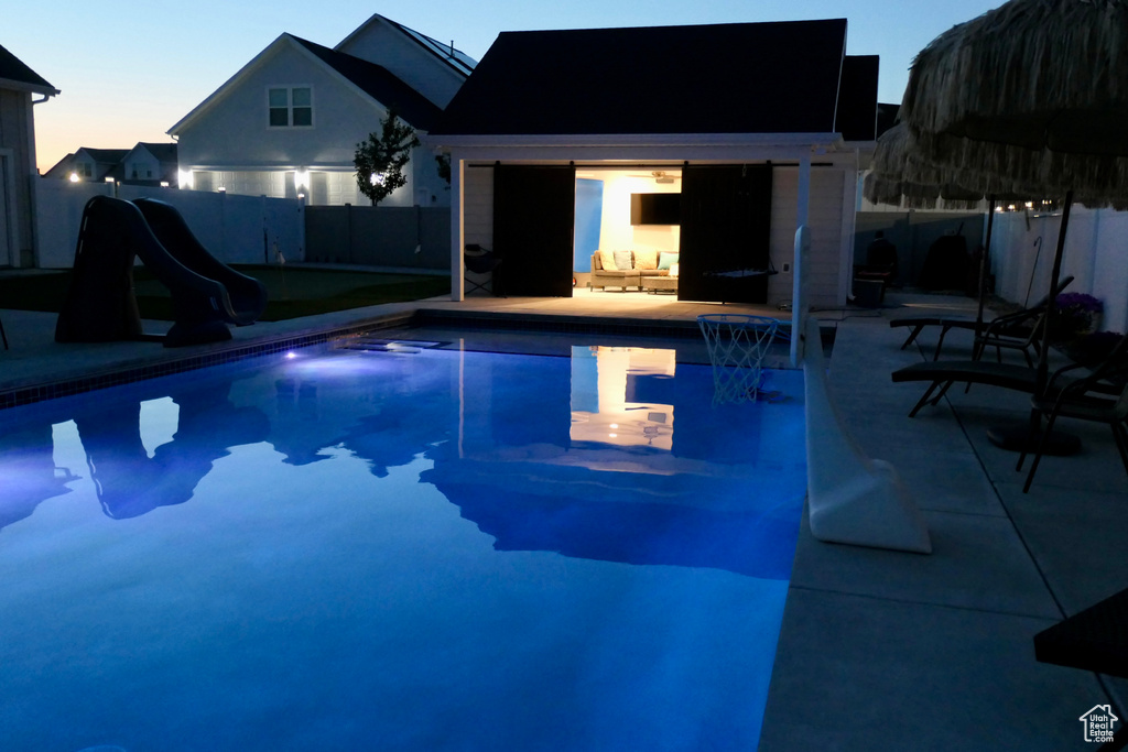 Pool at dusk with a water slide, a fenced backyard, and a patio