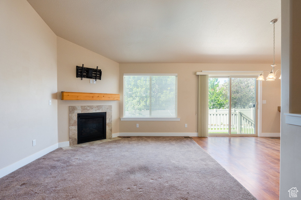 Unfurnished living room featuring plenty of natural light, a tiled fireplace, a chandelier, vaulted ceiling, and baseboards