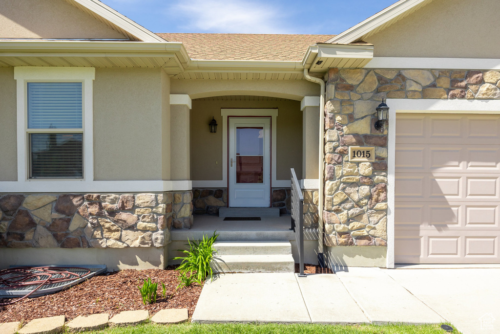 Entrance to property featuring stone siding, stucco siding, and an attached garage