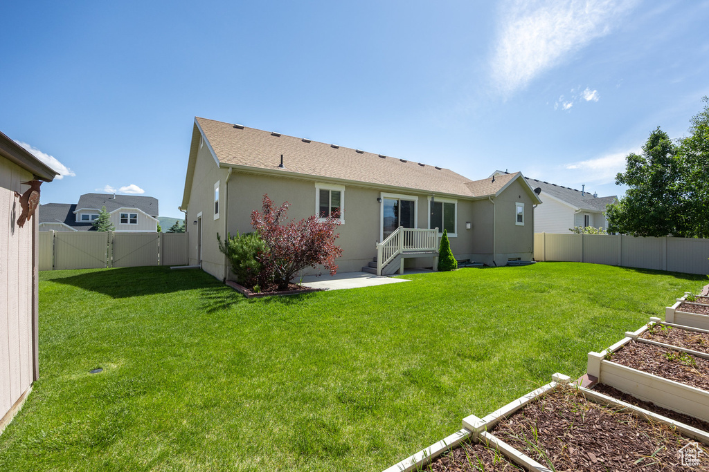 Back of house featuring a vegetable garden, a gate, stucco siding, and a patio