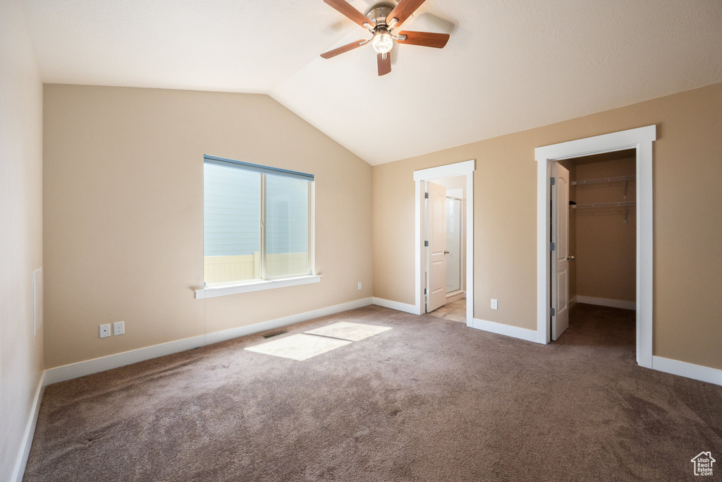 Unfurnished bedroom featuring carpet, vaulted ceiling, a spacious closet, ensuite bathroom, and a ceiling fan