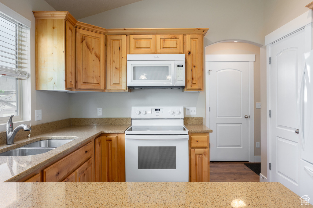Kitchen featuring white appliances, a sink, lofted ceiling, light stone counters, and dark wood-style floors