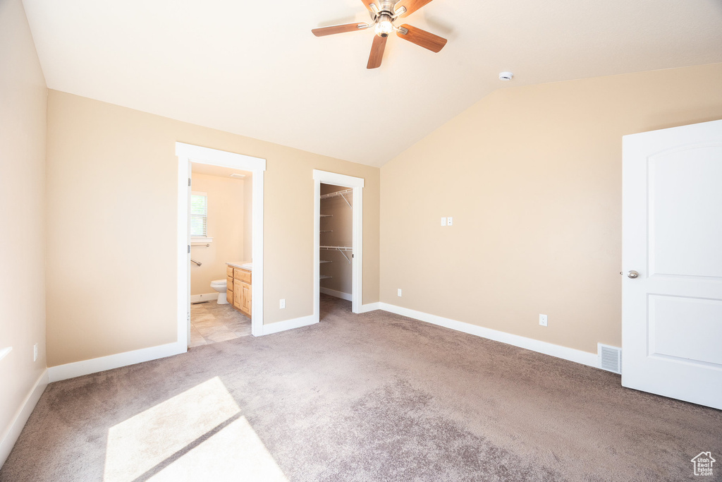 Unfurnished bedroom featuring light colored carpet, a walk in closet, vaulted ceiling, a closet, and connected bathroom
