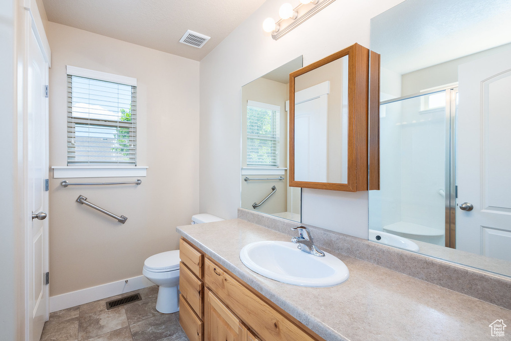 Full bathroom with baseboards, toilet, vanity, and a shower with shower door