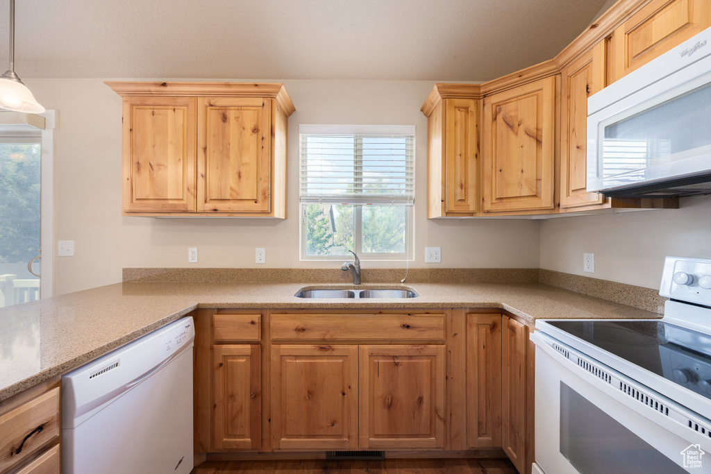 Kitchen with white appliances, a sink, light brown cabinets, and decorative light fixtures