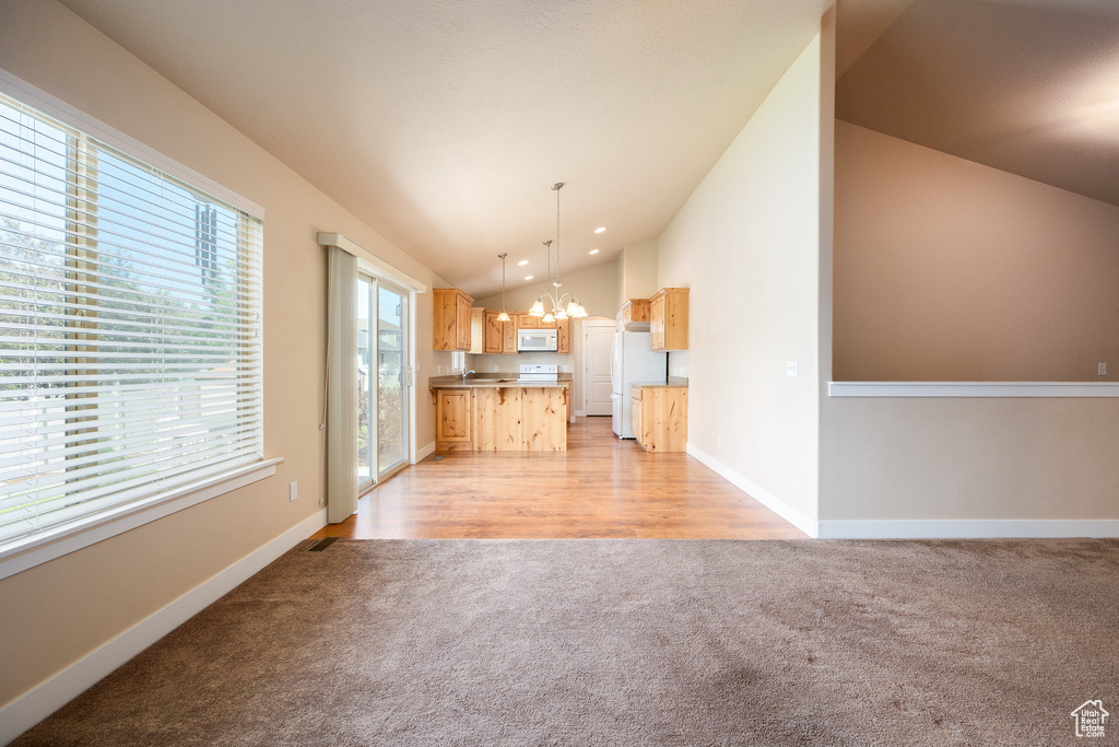 Unfurnished living room with light colored carpet, vaulted ceiling, a chandelier, and baseboards