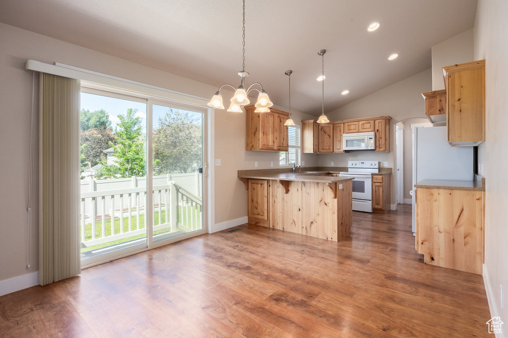 Kitchen featuring white appliances, a peninsula, a sink, wood finished floors, and lofted ceiling