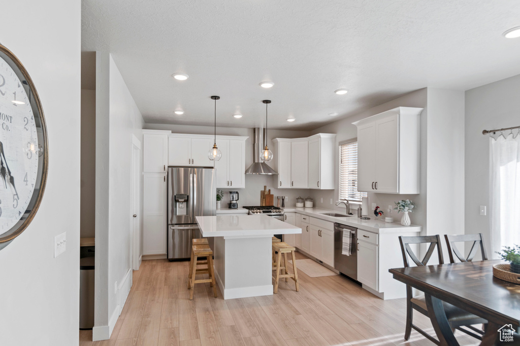 Kitchen featuring stainless steel appliances, a sink, a breakfast bar, light countertops, and light wood-type flooring