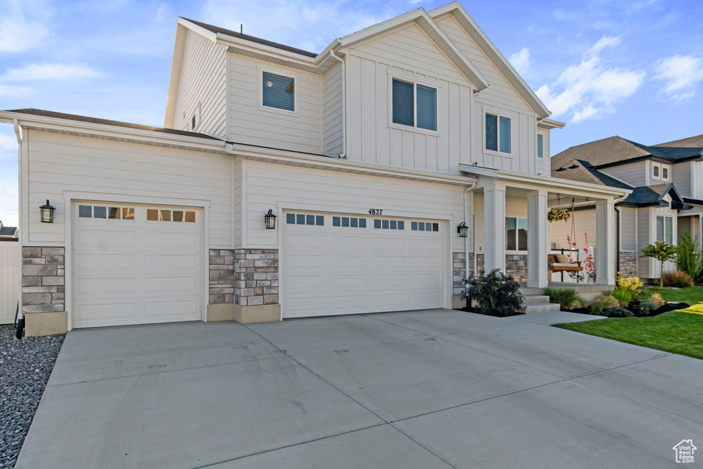 View of front of property with stone siding, board and batten siding, driveway, a porch, and a garage