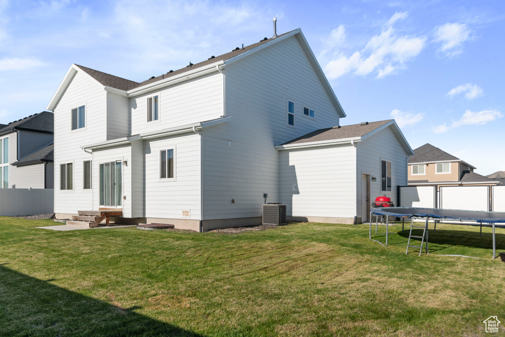 Back of property featuring a trampoline, central AC unit, a lawn, and entry steps
