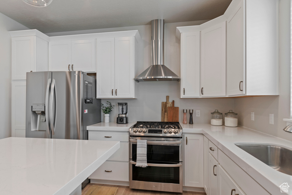 Kitchen with stainless steel appliances, wall chimney range hood, and white cabinets