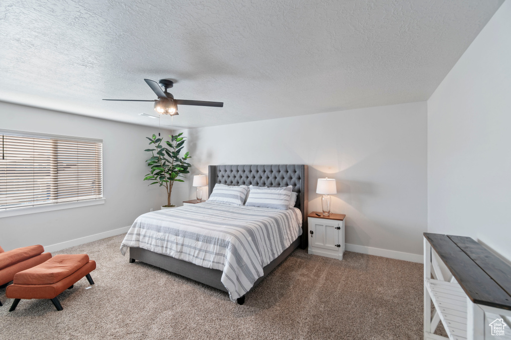 Carpeted bedroom with a textured ceiling, baseboards, and a ceiling fan