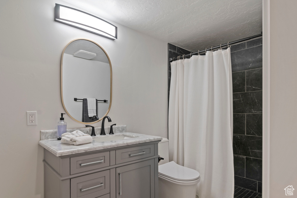 Bathroom featuring toilet, vanity, a textured ceiling, and tiled shower