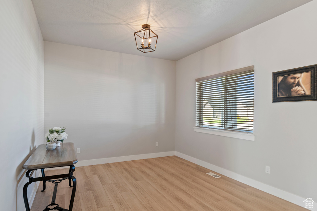 Unfurnished room featuring light wood-type flooring, a chandelier, and baseboards