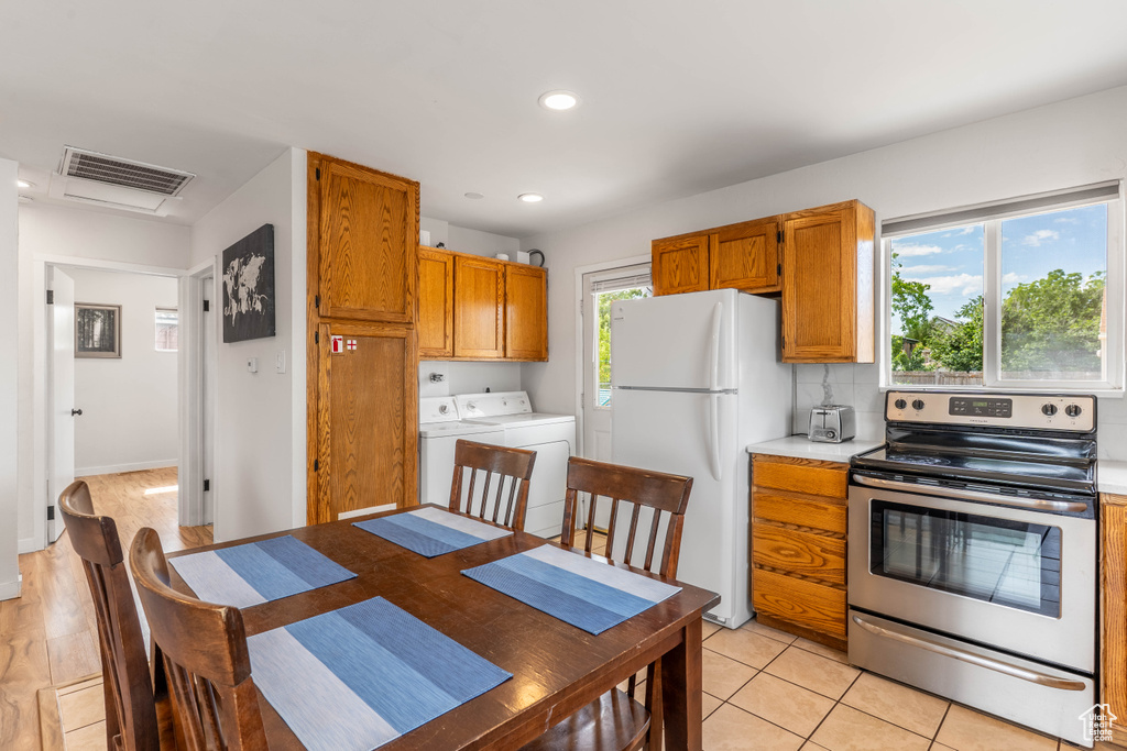 Kitchen with electric stove, freestanding refrigerator, independent washer and dryer, light countertops, and brown cabinets