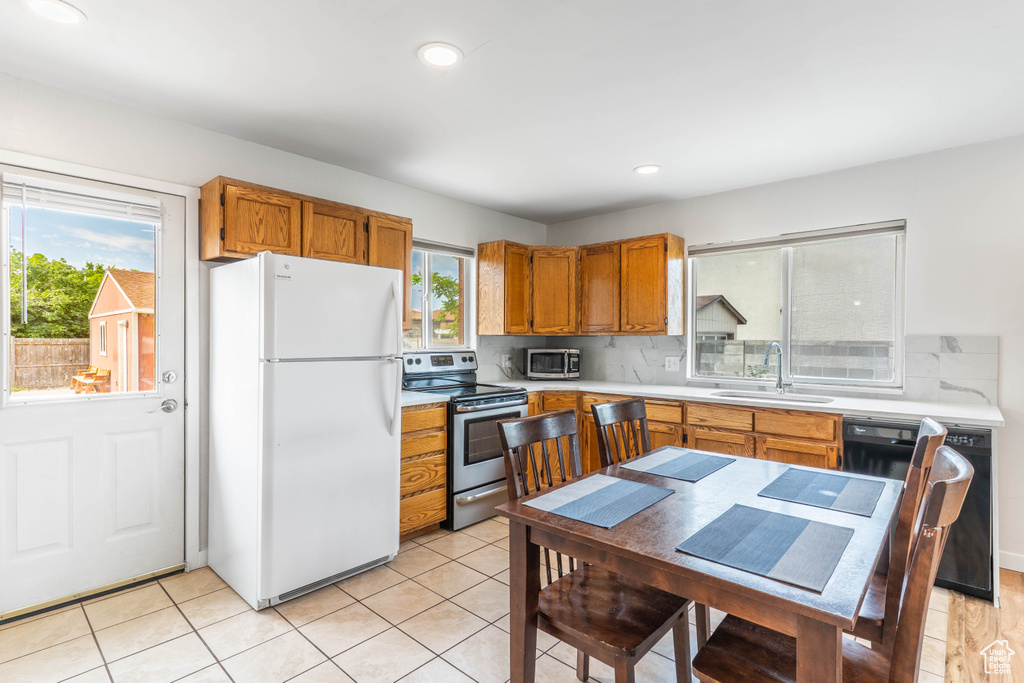 Kitchen featuring appliances with stainless steel finishes, a sink, light countertops, backsplash, and brown cabinetry