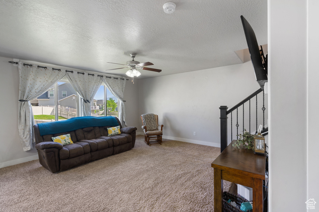 Carpeted living area with a textured ceiling, a ceiling fan, baseboards, and stairway