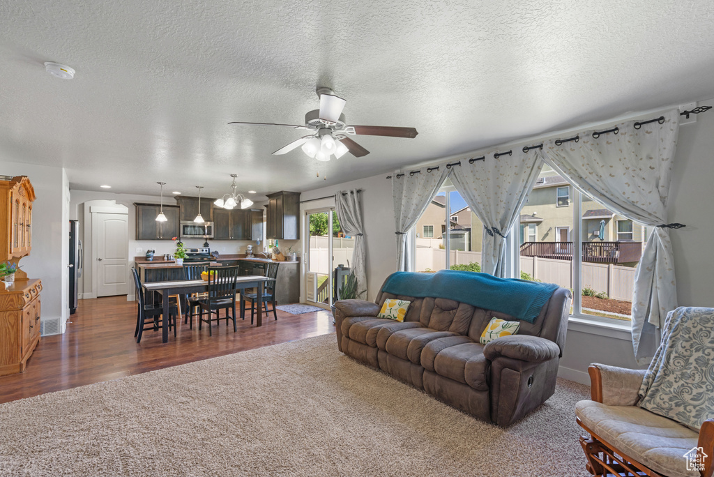 Carpeted living area featuring a ceiling fan, a chandelier, a textured ceiling, wood finished floors, and baseboards