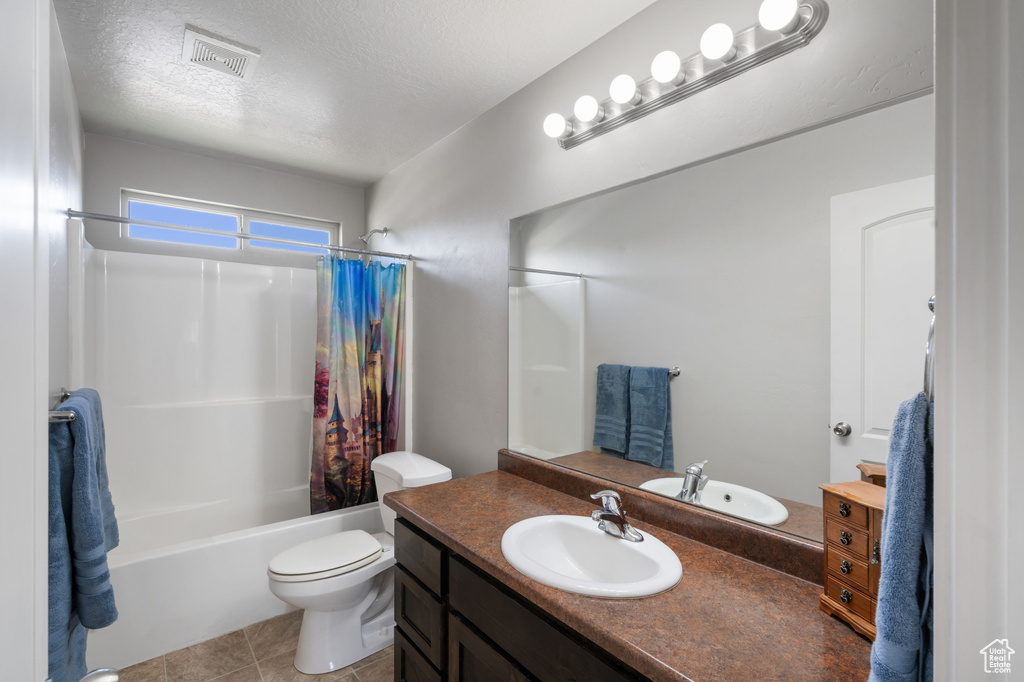 Bathroom featuring vanity, shower / tub combo with curtain, a textured ceiling, toilet, and tile patterned floors