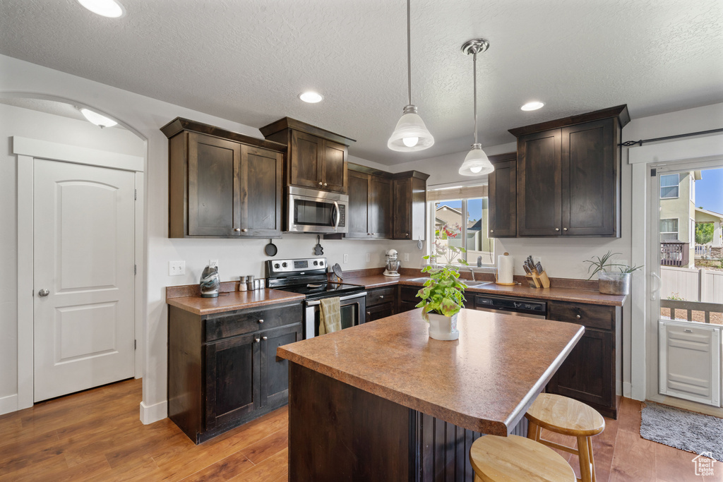 Kitchen with appliances with stainless steel finishes, dark brown cabinets, a kitchen bar, wood finished floors, and healthy amount of natural light