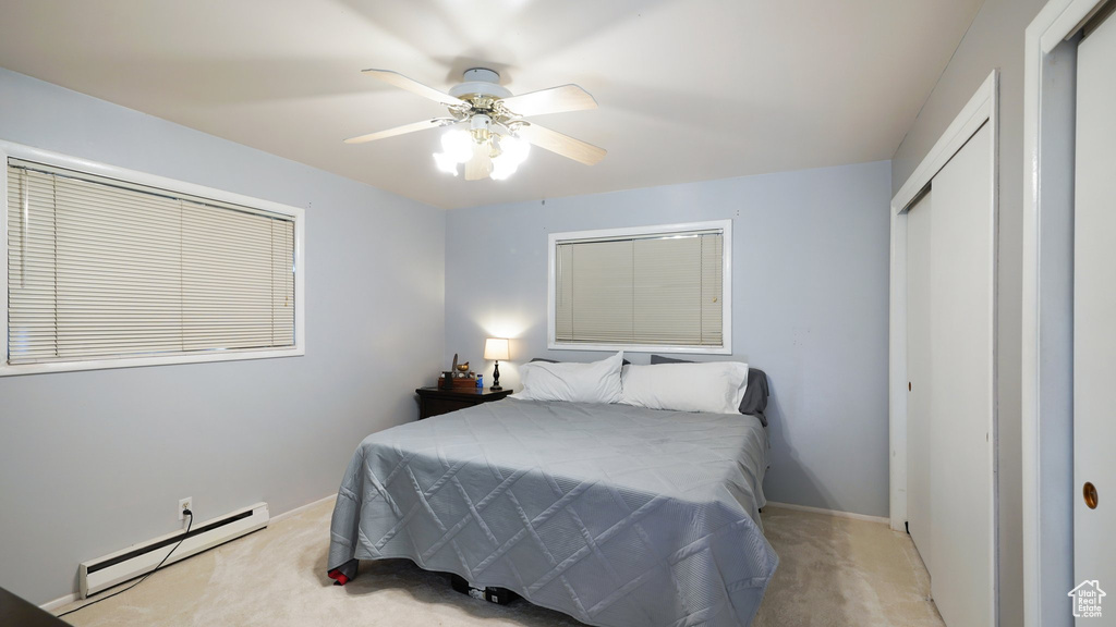 Carpeted bedroom featuring a baseboard radiator, a closet, baseboards, and a ceiling fan