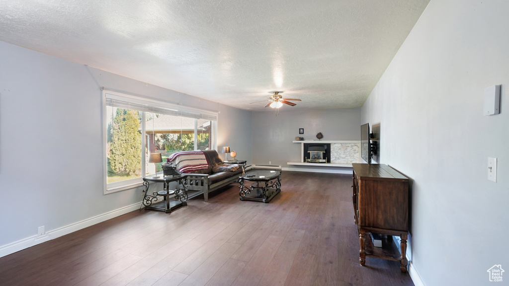 Living area with ceiling fan, a glass covered fireplace, a textured ceiling, dark wood-type flooring, and baseboards