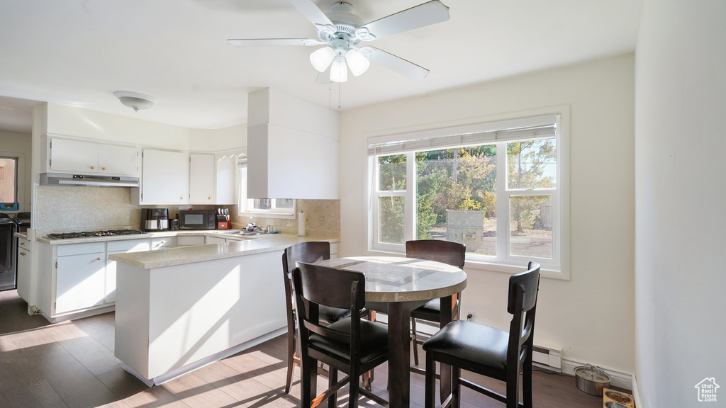 Kitchen with under cabinet range hood, black microwave, a peninsula, and tasteful backsplash