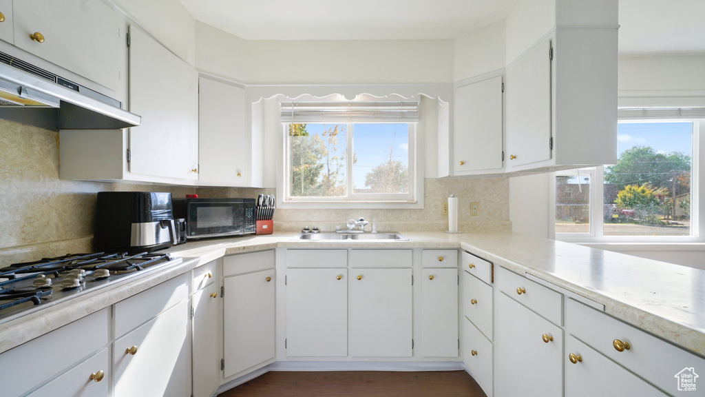 Kitchen featuring black microwave, under cabinet range hood, a sink, stainless steel gas cooktop, and backsplash