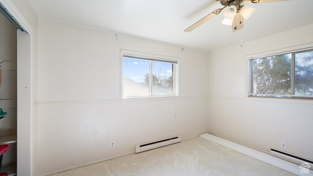 Carpeted empty room featuring a baseboard radiator, healthy amount of natural light, and a ceiling fan