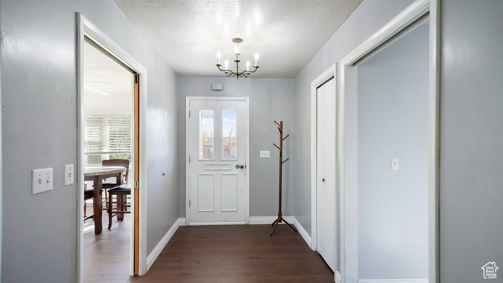 Foyer entrance featuring a chandelier, dark wood finished floors, a textured ceiling, and baseboards