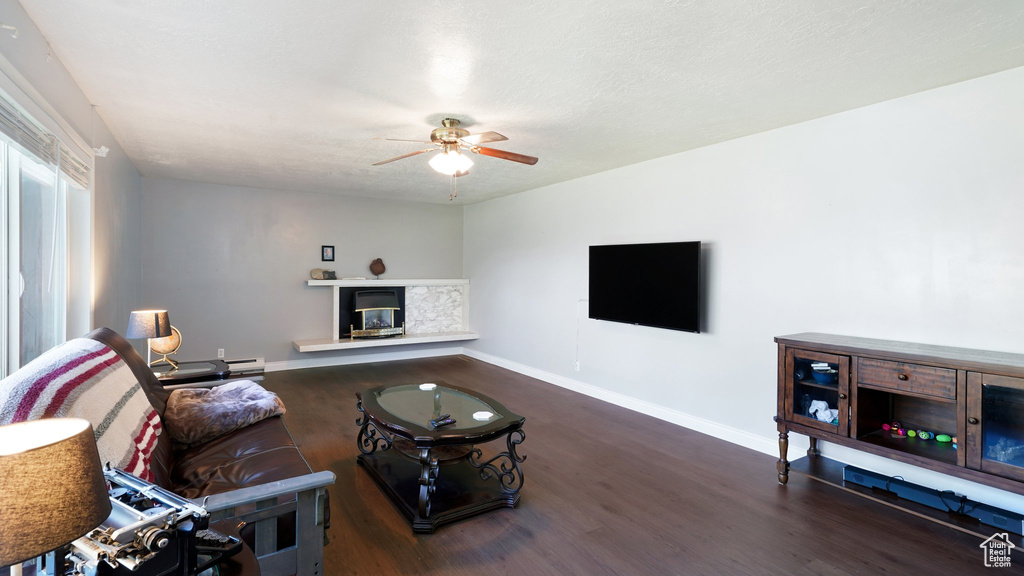 Living room with ceiling fan, wood finished floors, a glass covered fireplace, and baseboards