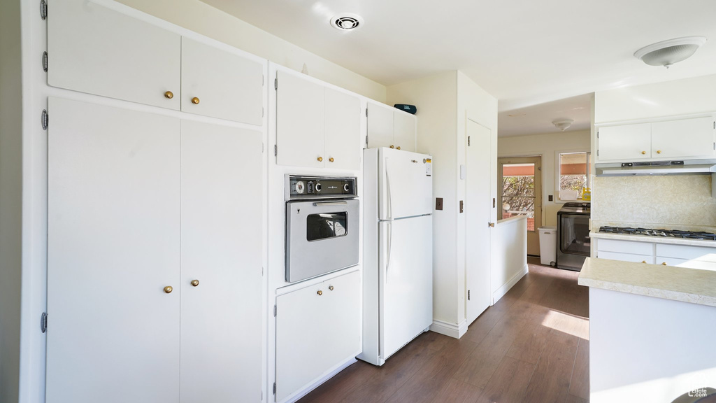 Kitchen with white appliances, under cabinet range hood, dark wood finished floors, light countertops, and white cabinetry