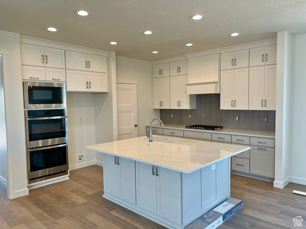 Kitchen featuring stainless steel appliances, wood finished floors, white cabinetry, recessed lighting, and a textured ceiling