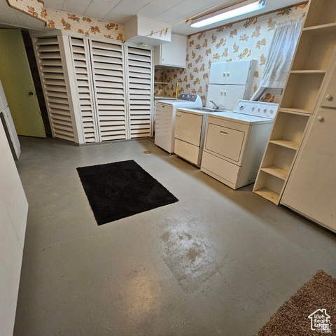 Laundry room featuring independent washer and dryer, wallpapered walls, and cabinet space