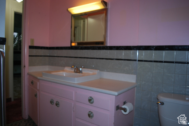 Bathroom featuring tile walls, toilet, vanity, and a wainscoted wall