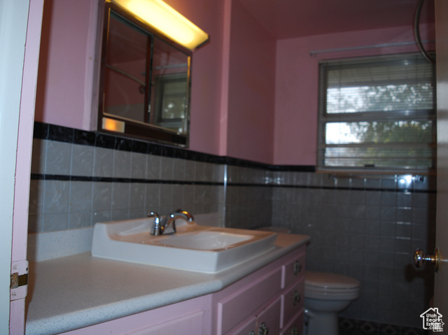 Bathroom with toilet, vanity, tile walls, and a wainscoted wall