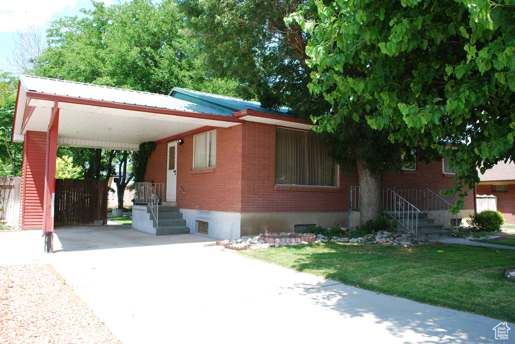 View of front of property with driveway, brick siding, an attached carport, and metal roof
