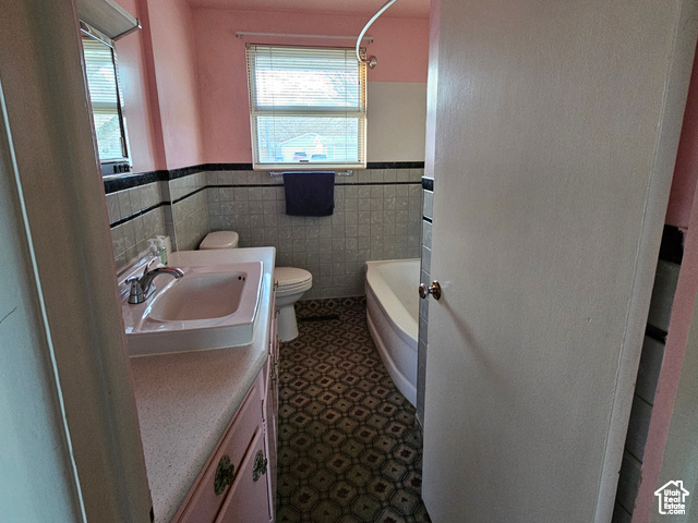 Full bathroom with toilet, vanity, wainscoting, tile walls, and washtub / shower combination