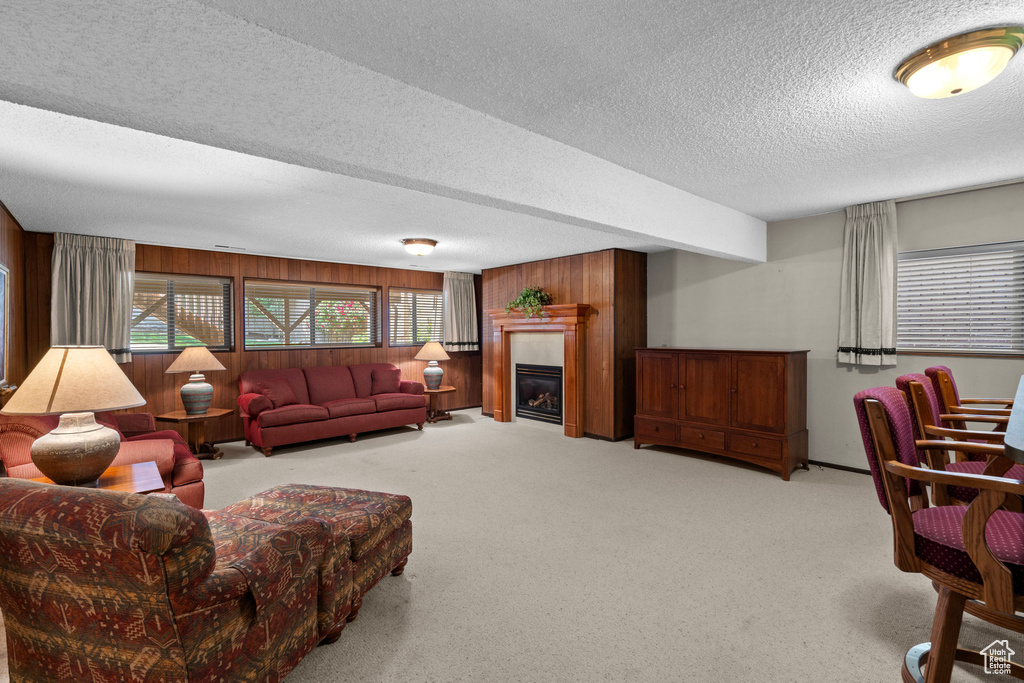 Living area featuring a textured ceiling, wooden walls, light colored carpet, and a glass covered fireplace