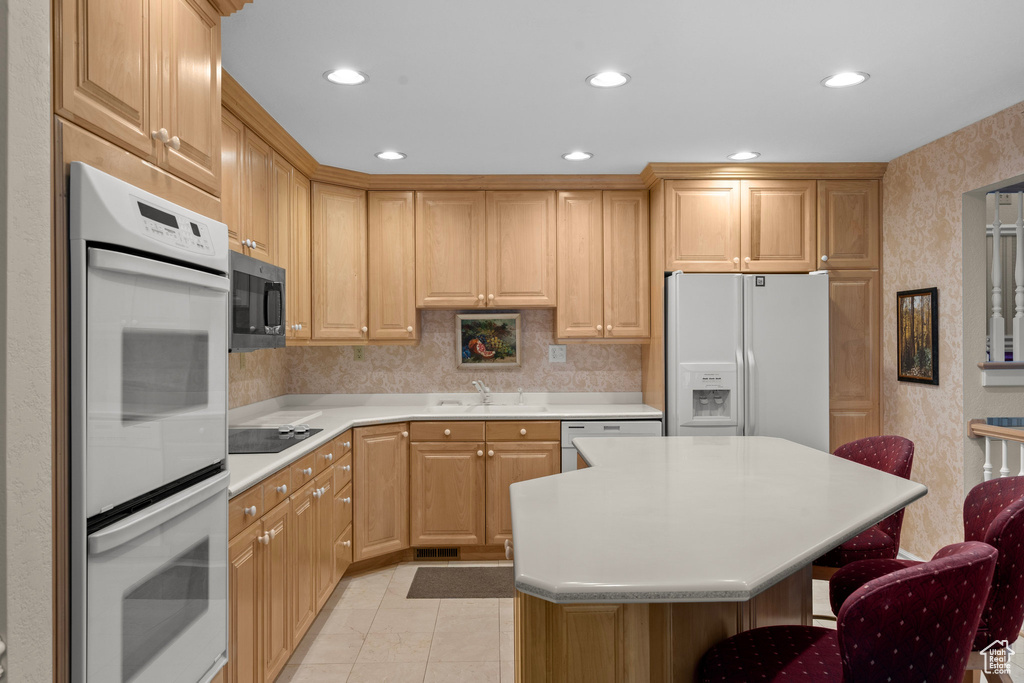 Kitchen featuring white appliances, a kitchen breakfast bar, light countertops, recessed lighting, and light brown cabinets
