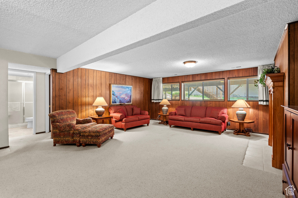 Living room featuring wood walls, a textured ceiling, light carpet, and beam ceiling