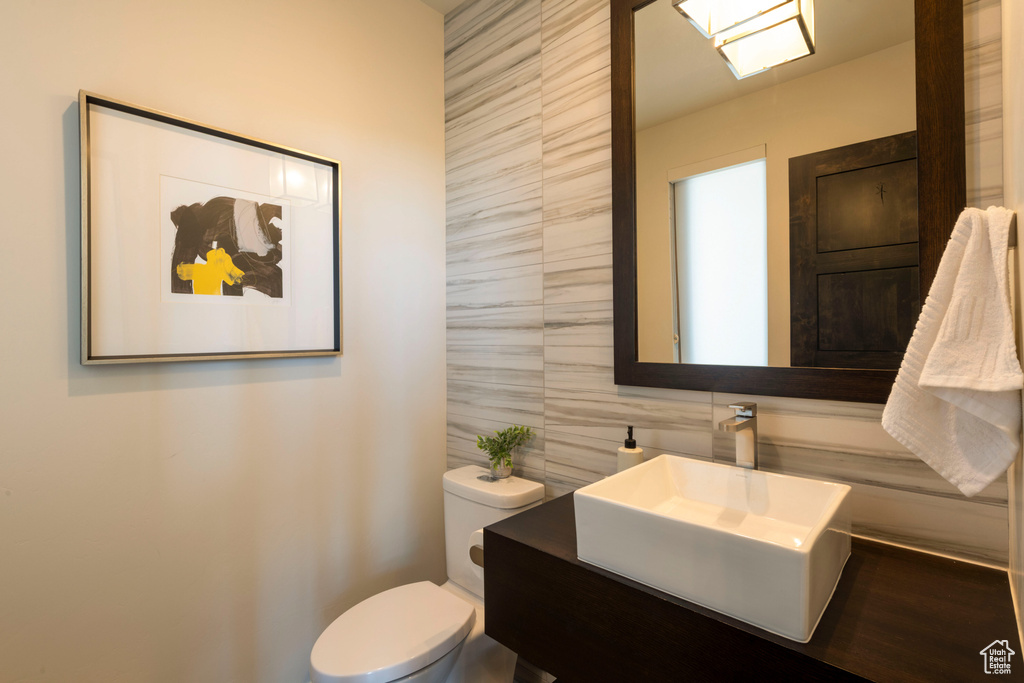 Bathroom with tile walls, toilet, vanity, and decorative backsplash