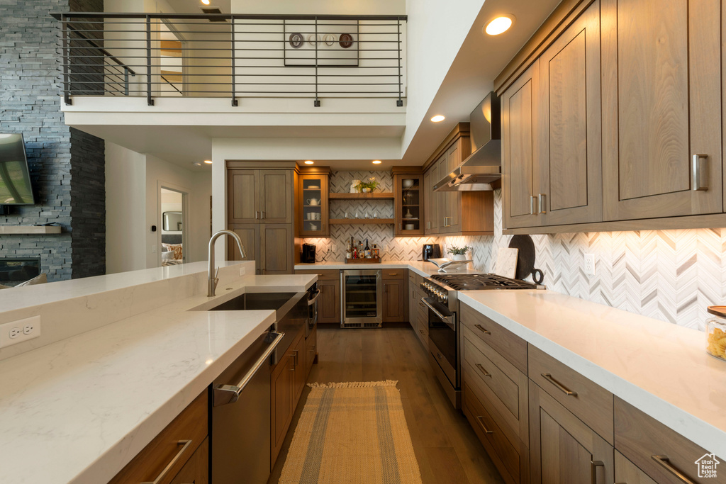 Kitchen with wall chimney exhaust hood, appliances with stainless steel finishes, beverage cooler, wood finished floors, and a sink