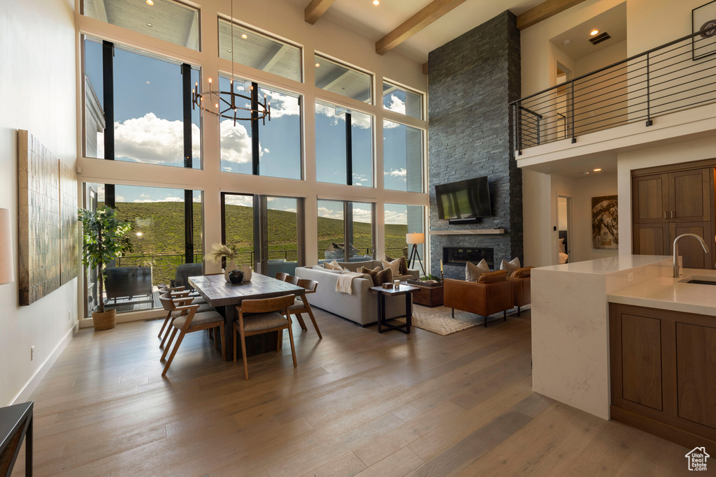 Dining area featuring a towering ceiling, wood finished floors, a fireplace, beamed ceiling, and a chandelier