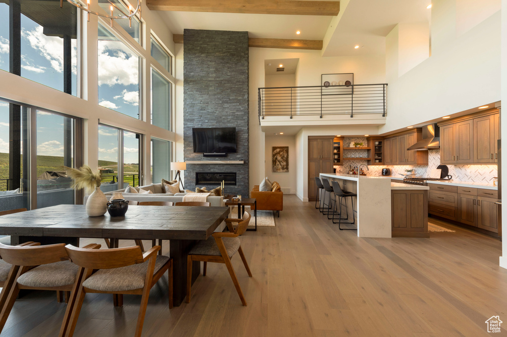 Dining area with a towering ceiling, light wood-type flooring, a stone fireplace, beam ceiling, and recessed lighting