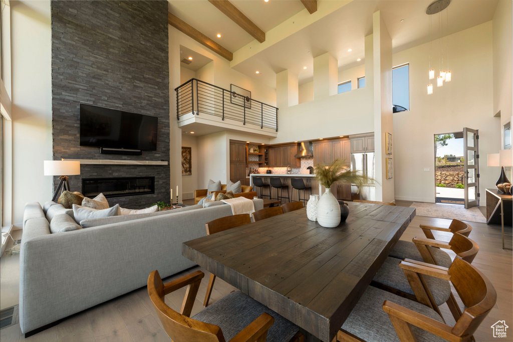 Dining room with a towering ceiling, a stone fireplace, light wood finished floors, and beam ceiling
